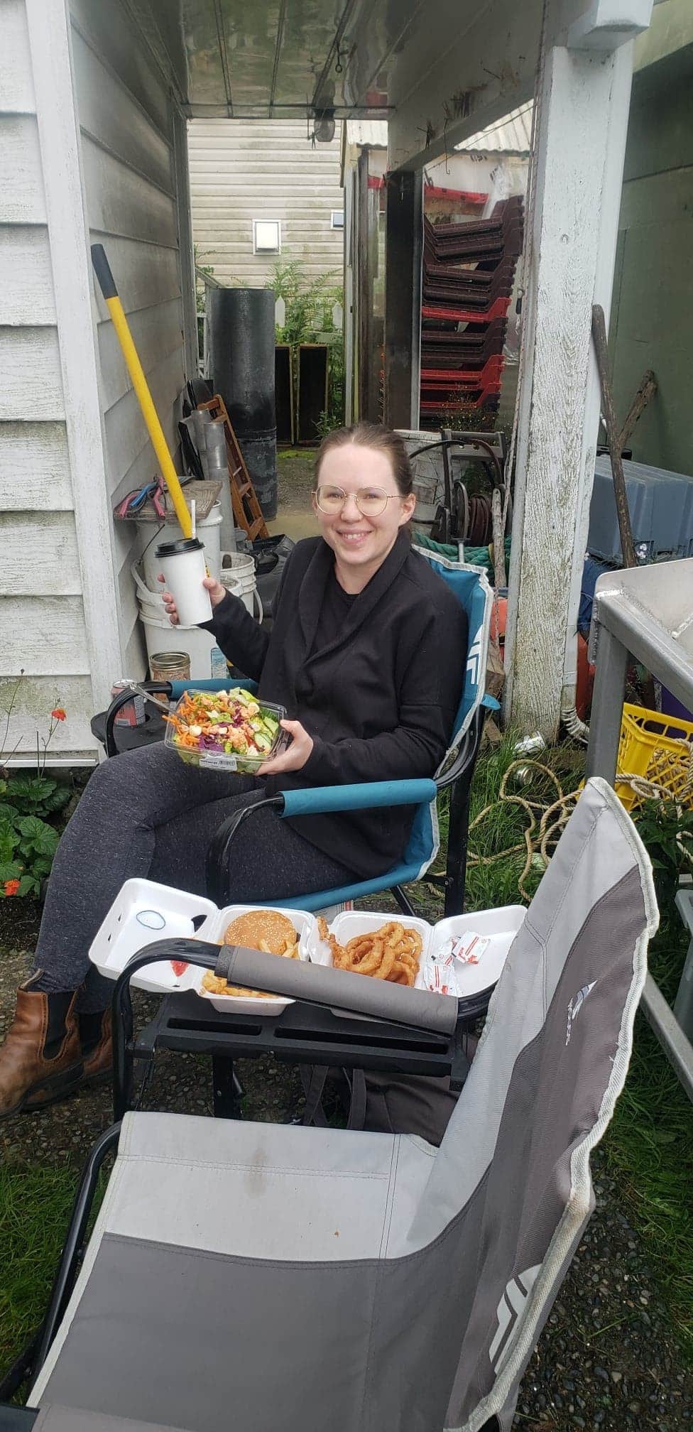 A lady sitting a chair and holding a cup and food